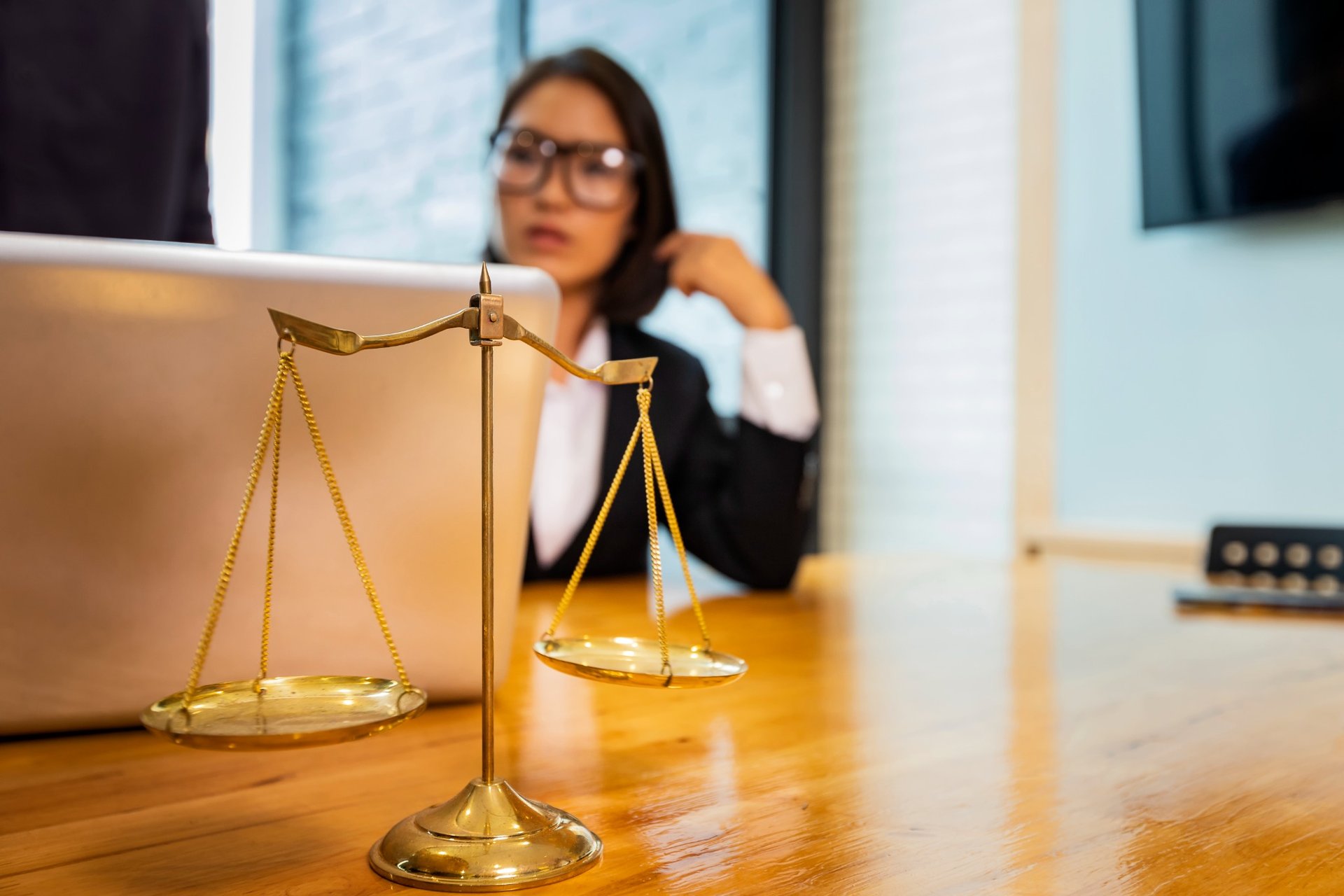 Brass justice scales on a desk with lawyer working in the background