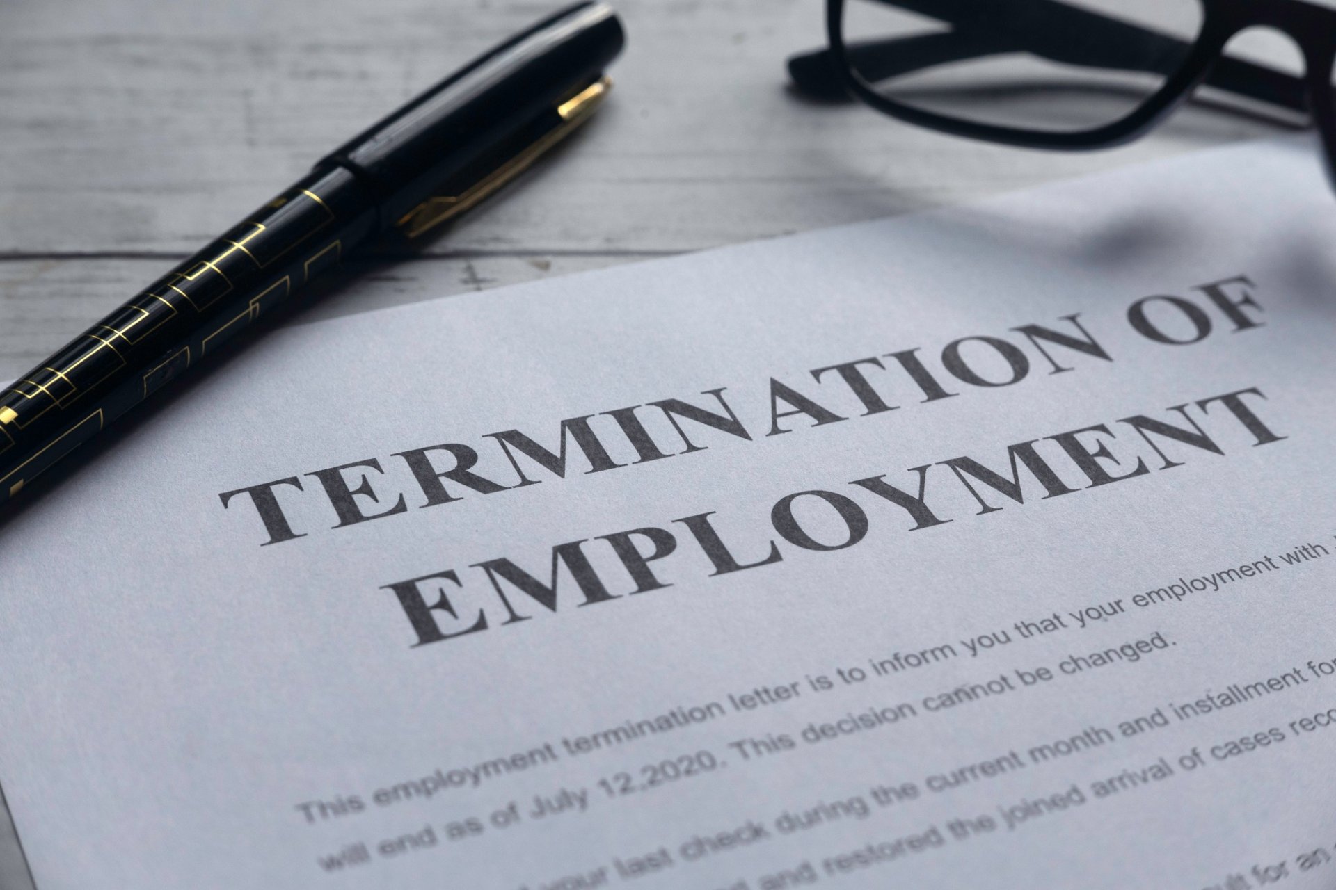 Close-up of termination of employment letter with glasses and pen