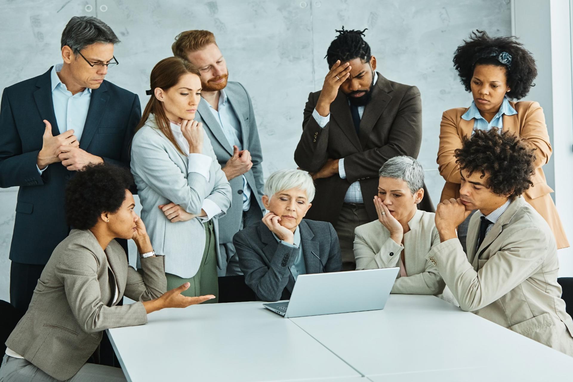 Group of business professionals gathered around a laptop in a casual office setting