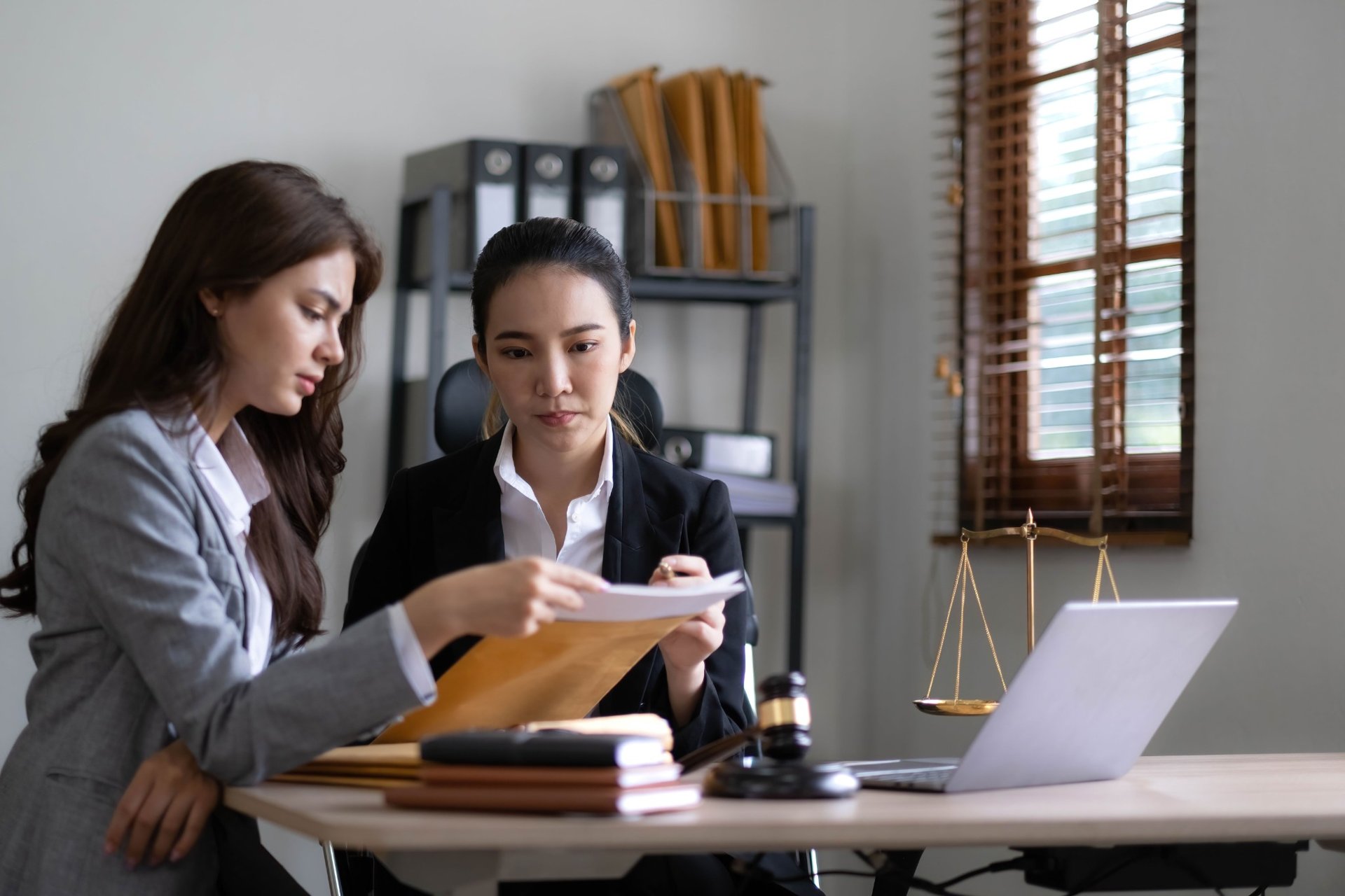 Two businesswomen in formal attire reviewing documents in a law office setting