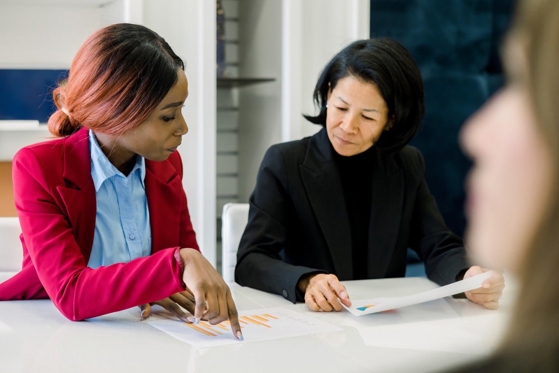 Two businesswomen reviewing charts together during a team meeting