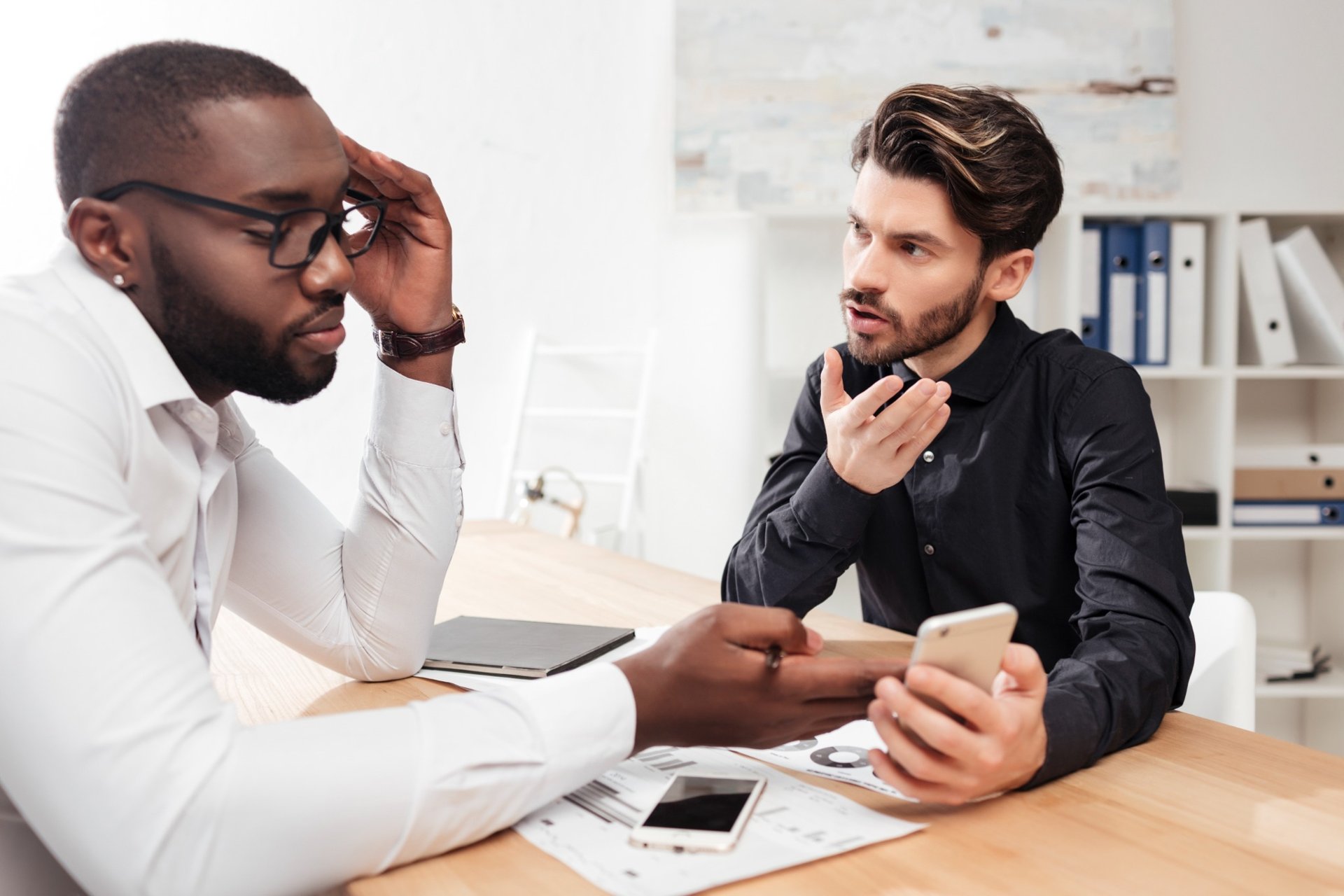 Two male professionals engaged in a serious discussion at an office desk