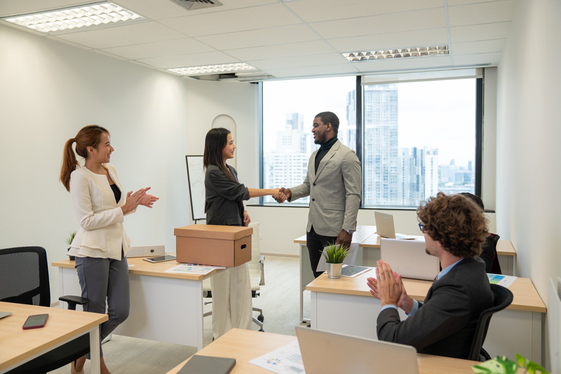 Woman shakes hands with colleague while others applaud in modern office